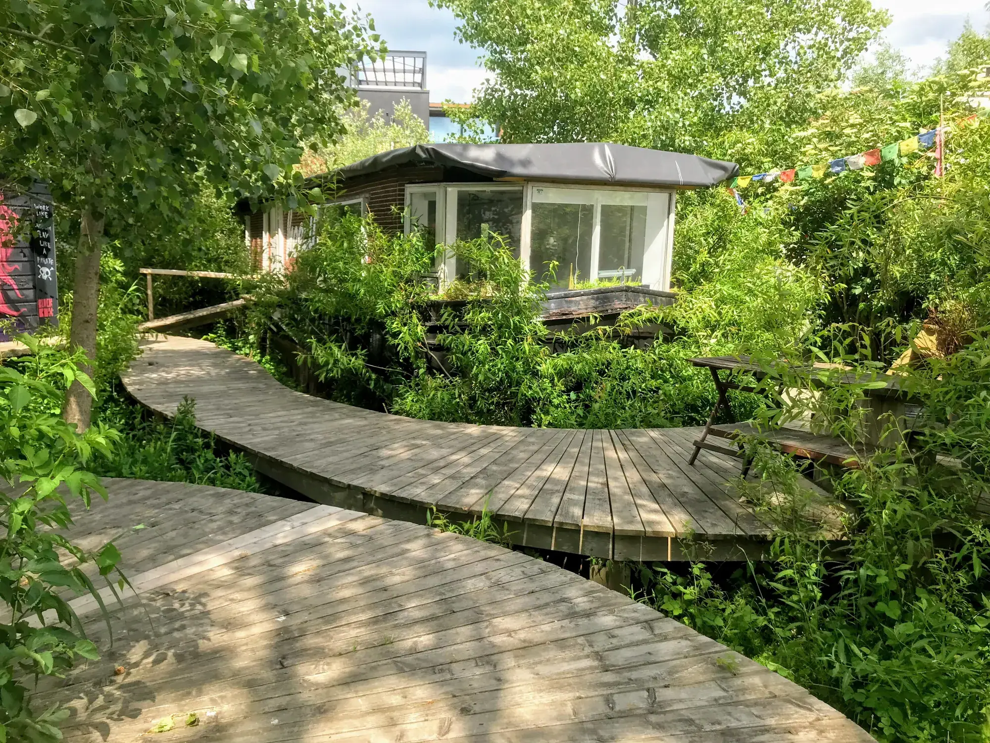 La passerelle en bois serpente au-dessus du sol pollué, entre les ateliers.