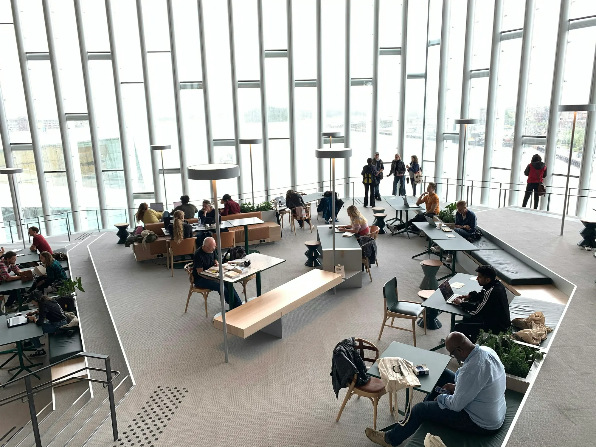 Lecteurs aux tables de travail de Deichman Bjørvika, devant de hautes baies vitrées